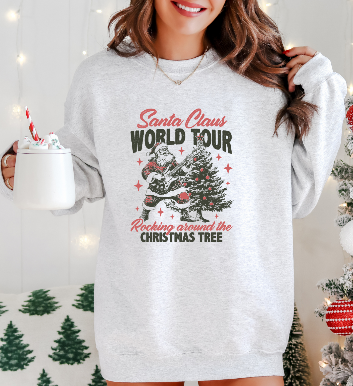 Woman wearing a Christmas-themed sweatshirt with a tree and Santa Claus design, holding a hot chocolate mug.